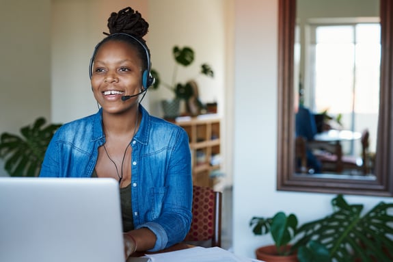 Woman on computer wearing headset smiling while working.